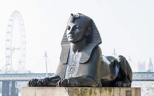Bronze Egyptian sphinx statue on the Thames embankment, with The London Eye, Golden Jubilee Bridge and Big Ben in the background, London, England