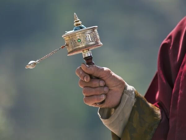 A Buddhist spins his hand-held prayer wheel in a clockwise direction with the help of a weighted chain attached to it. Each turn is the equivalent of reading the prayers or