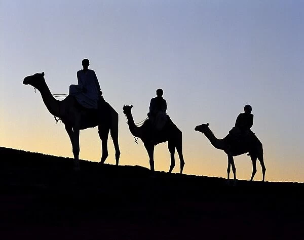 Three camel riders silhouetted against an evening sky