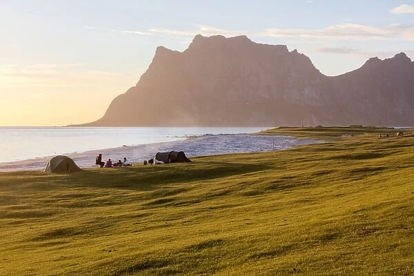 Camping tents on green meadows next to sea lighted up by midnight sun Uttakleiv Lofoten
