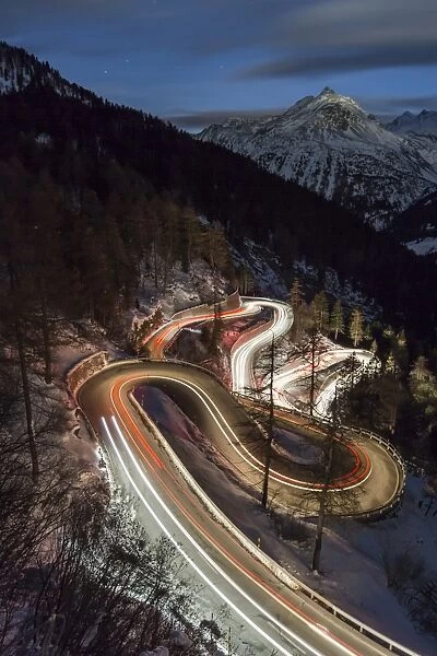 Car lights on the curvy Maloja Pass road at night. Maloja Pass, Engadin, Graubunden