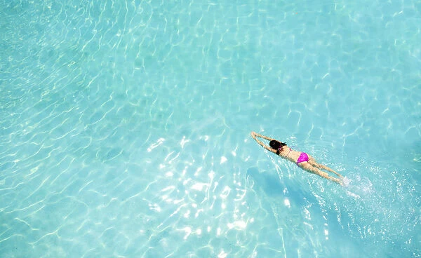 Central America, Belize, Cayo, a girl in a pink bikini swimming in a blue swimming pool