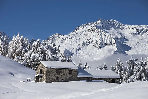 Chalet at Granda alp in winter, in the background Desenigo peak, Retiche alps, Lombardy