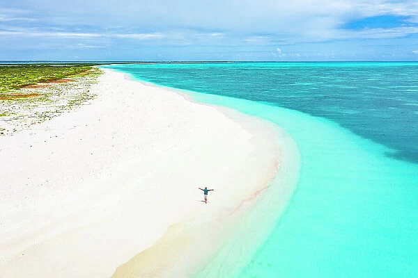 Cheerful man with arms outstretched admiring the sea standing on a white sand beach, aerial view, Antigua & Barbuda, Caribbean (MR)