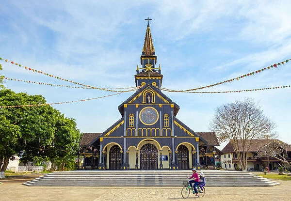 Childen ride a biycycle in front of Kon Tum Cathedral, also known as Wooden Church