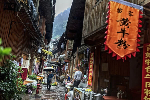China, Hunan province, Fenghuang, old woman carrying food along the narrow streets