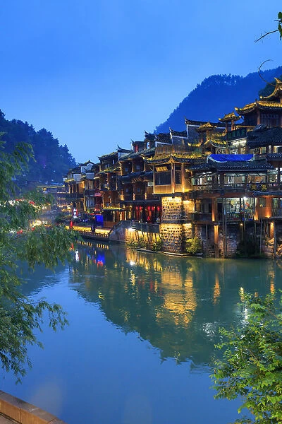 China, Hunan province, Fenghuang, riverside houses by night reflecting in the river