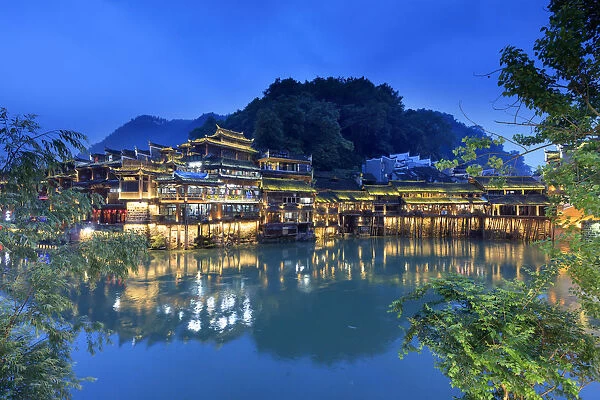 China, Hunan province, Fenghuang, riverside houses by night reflecting in the river