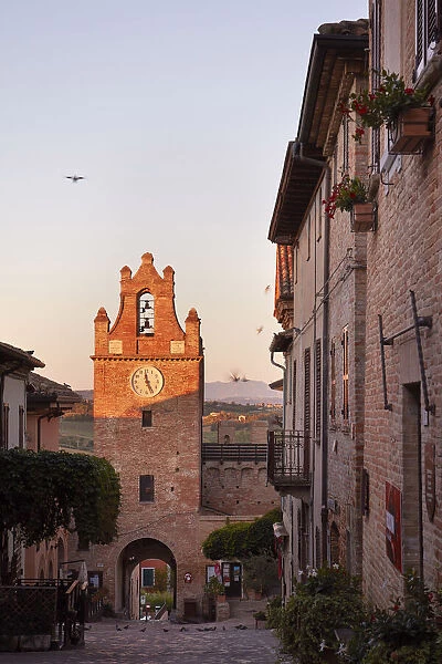 The clock tower of the medieval village of Gradara at sunrise with the hills in