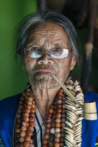 Close-up portrait of old lady with glasses and traditional facial tattoo smoking a pipe