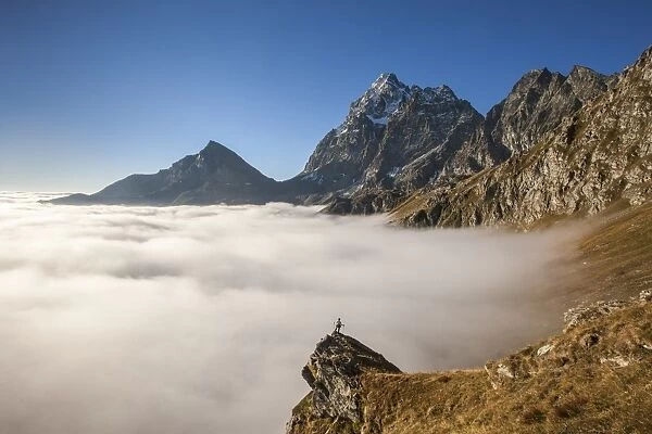A clouds sea, in autumn, under Monviso peak and Viso Mozzo peak, with an alpinist on a pulpit rock