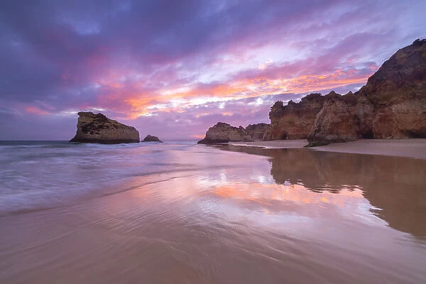 A colorful sunset reflected on the wet shores of Praia Dos Tres Irmaos
