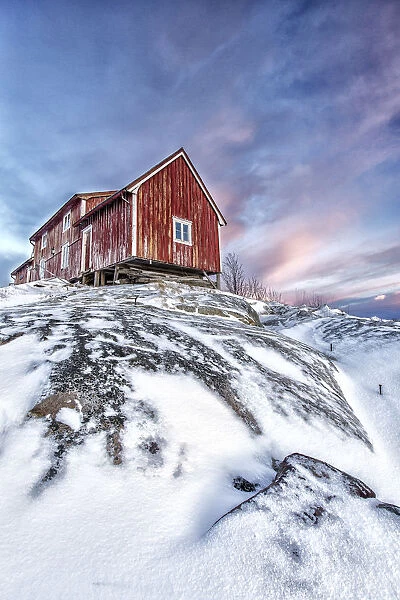 The colors of dawn light up the sky above a typical red house of Henningsvaer