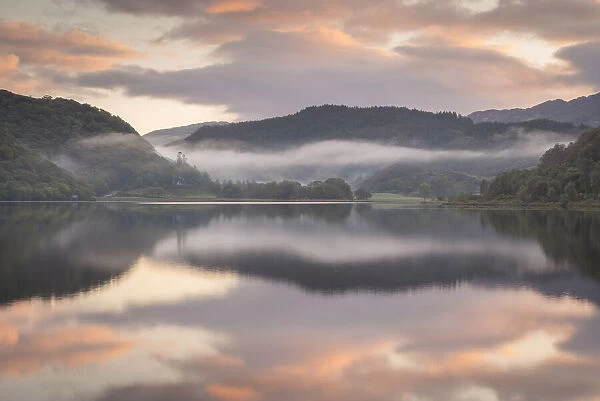 Colourful dawn sky above a reflective and misty Llyn Dinas, Snowdonia National Park