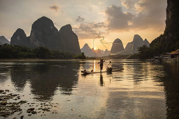 Cormorant fisherman throwing net on Li River at dawn, Xingping, Yangshuo, Guangxi, China