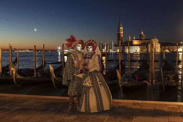 A couple in costume during the Venice Carnival posing in front of Venice lagoon, Venice