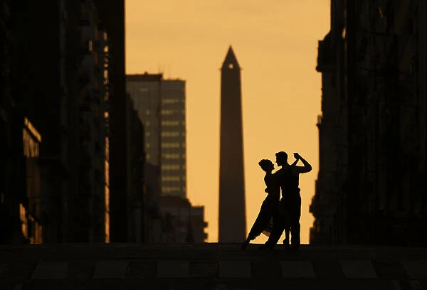 A couple of Professional Tango dancers on Avenida Corrientes at sunset, with the Obelisk monument in the background. Buenos Aires, Argentina. (MR)