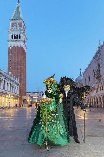 A couple wearing masks and Venetian costume stand in St Marks square during the