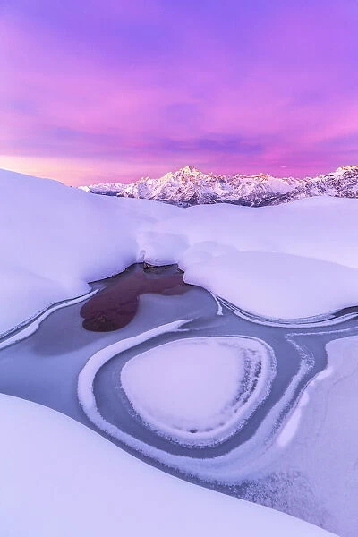 Crazy shape in a frozen alpine lake at sunrise with view on Mount Disgrazia