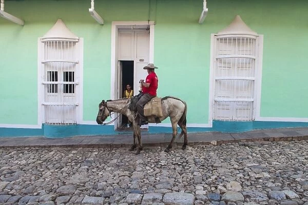 Cuba, Trinidad, Milkman on horseback delivers bottles of milk to house