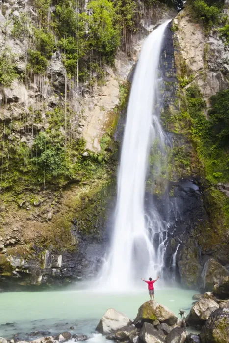 Framed Print : Dominica, Delices. A man stands at the base of Victoria Falls, one of the tallest
