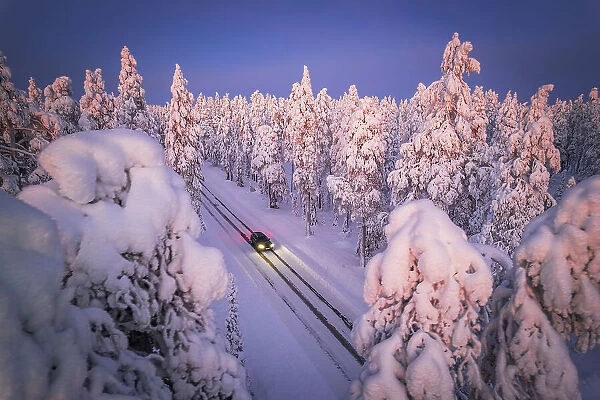 Drone a car with headlight on travelling the icy slippery road crossing the forest covered with snow, Muonio, Lapland, Finland
