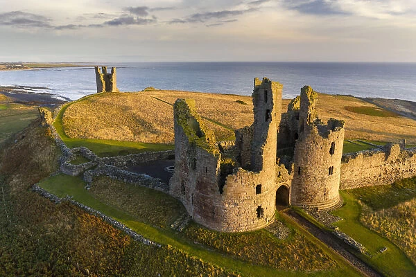 Dunstanburgh Castle's great gatehouse and Lilburn Tower illuminated in early morning