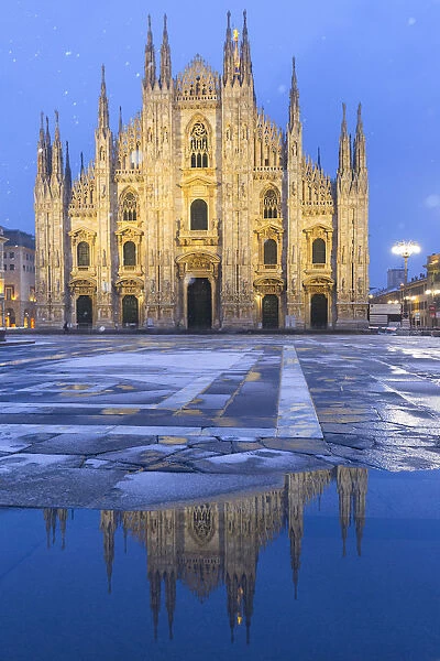 Duomo of Milan is reflected in a puddle during a snowfall at twilight. Milan, Lombardy