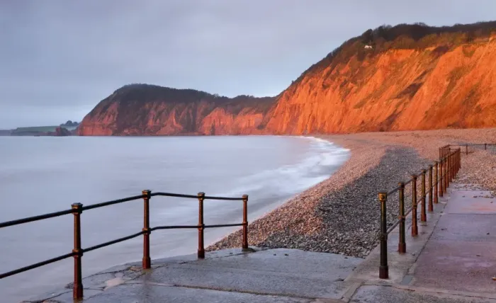 Framed Print : Early morning sunlight glows against the distinctive red cliffs of High Peak, viewed