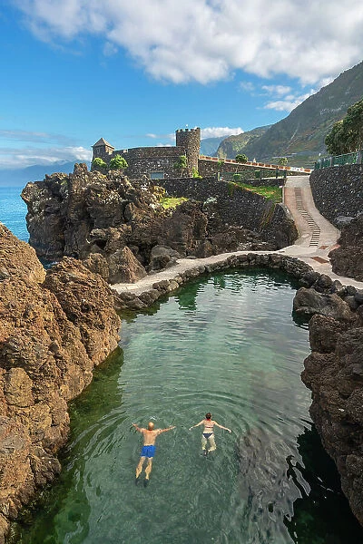 Elevated view of couple swimming in natural volcanic rock pools near Aquarium of Madeira (Aquario da Madeira), Porto Moniz, Madeira, Portugal