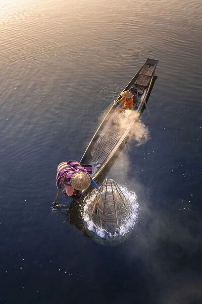 Elevated view of fisherman catching fish from boat using traditional conical net at