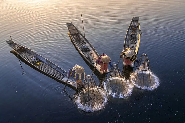 Elevated view of three fishermen catching fish from boats using traditional conical nets