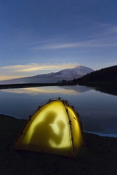 Etna erupting, is reflected in a lake at night on the Nebrodi muntains in the north of Sicily