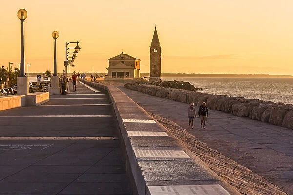 Europe, Italy, Veneto, Caorle. People walking at sunrise on the waterfront