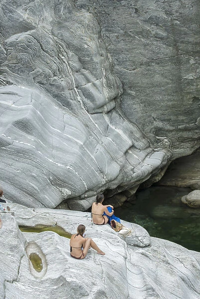 Europe, Switzerland, Ticino, Maggia Valley, two women in swim suits sitting on rocks