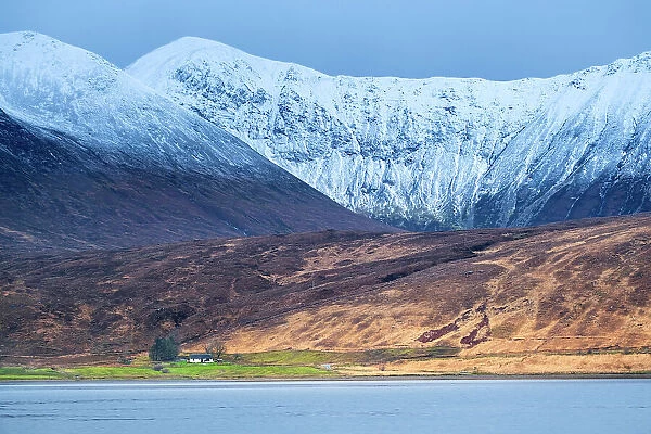 Europe, UK, Scotland, Isle of Skye, crofters cottage set against dramatic snowy mountains and a sea loch