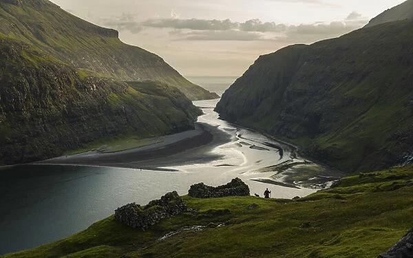 A farmer and his dog walking along the lagoon in Saksun. Streymoy, Faroe Islands