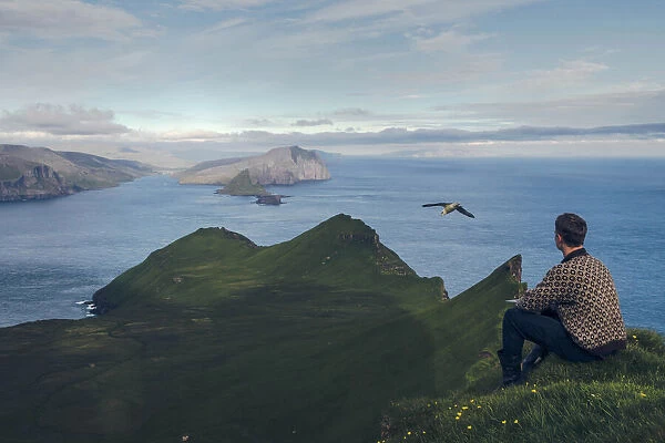 Faroese guy sitting along Knukur mountain in Mykines. Faroe Islands