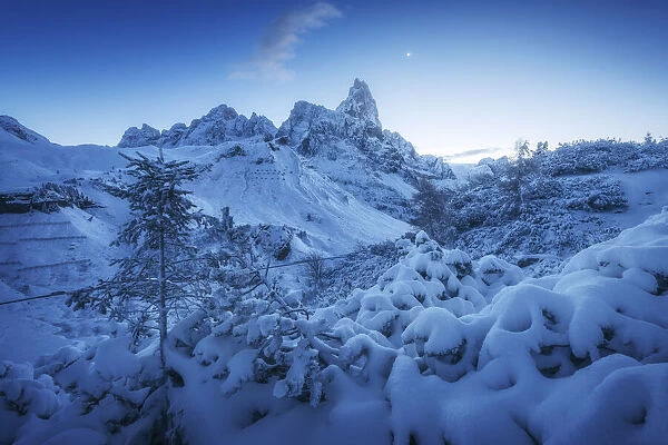 The first snow of the year in late autumn at Rolle Pass, with the majestic Pale di San Martino in the background and the rising moon in the sky. Dolomites, Italy