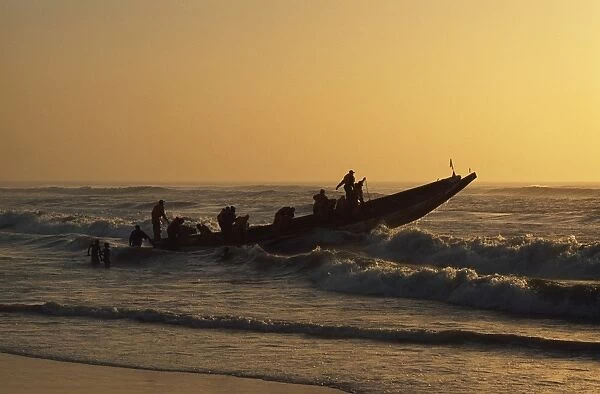 Fishermen launch their boat into the Atlantic Ocean at sunset
