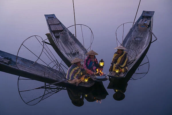 Three fishermen sitting on their boats warming up around a fire before sunrise, Lake Inle