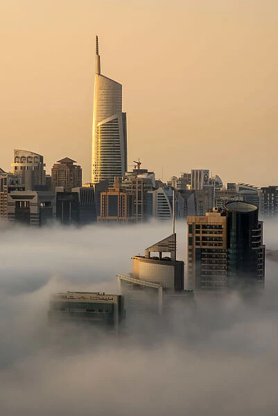 Foggy sunrise with Dubai Marins skyscrapers towering over the low clouds, Dubai