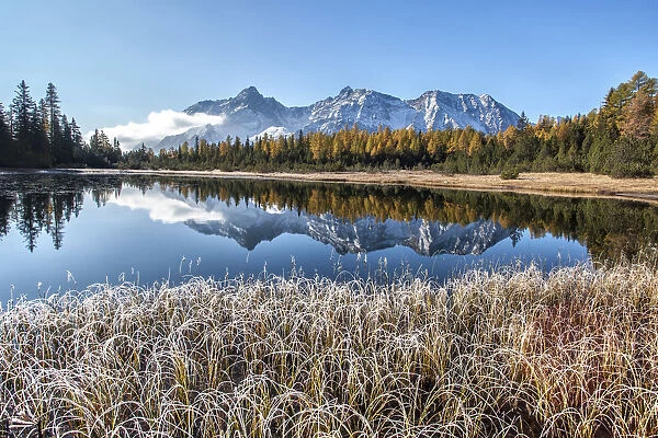 Frost and autumn colours at Entova Lake with snowy peaks reflected in the blue waters
