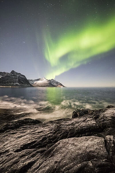 Frozen sea and rocky peaks illuminated by Northern Lights, Tungeneset, Senja, Tromso