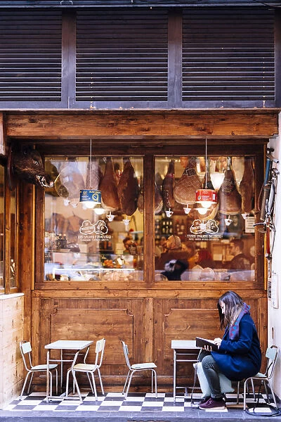 Girl reading in front of a traditional Salumeria in Bologna, Emilia Romagna, Italy