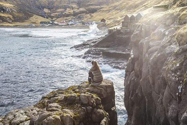 Girl sitting along the fjord close to Tjornuvik. Streymoy island, Faroe islands
