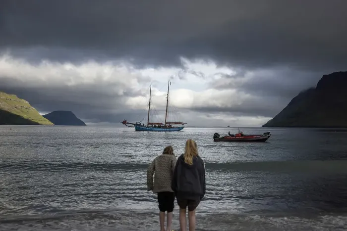 Framed Print : Two girls at G! Festival in Syðrugota walking into the ocean. In the background the sailship Norðlysið. Island of Eysturoy. Faroe Islands