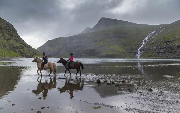 Girls riding horses in the lagoon in Saksun. Streymoy, Faroe Islands