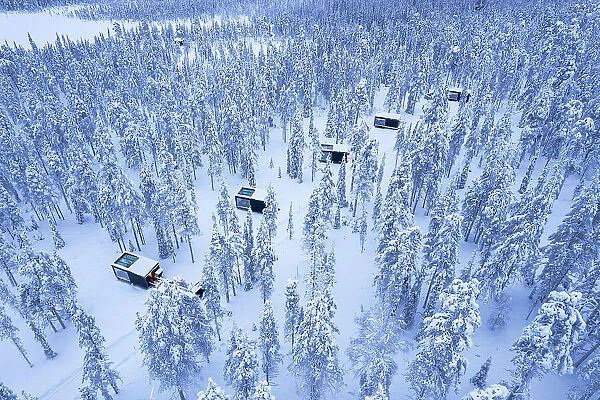 Glass cabins set on the middle of the frozen forest covered with snow at dusk, Finnish Lapland, Finland