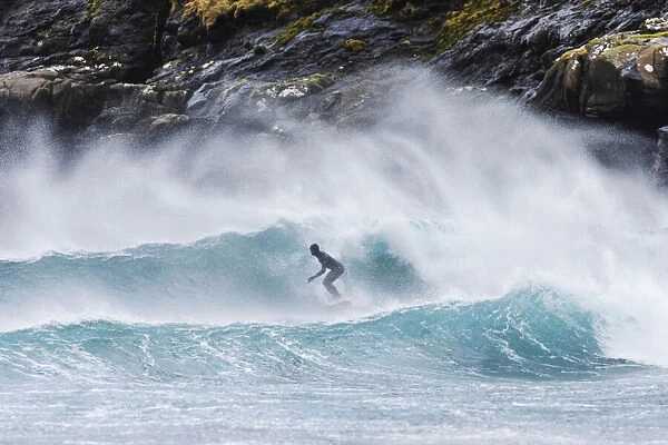 A guy surfing along the coast in front of Tjornuvik. Streymoy, Faroe Islands